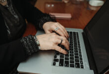 Close-up of hands typing on a laptop at a wooden table