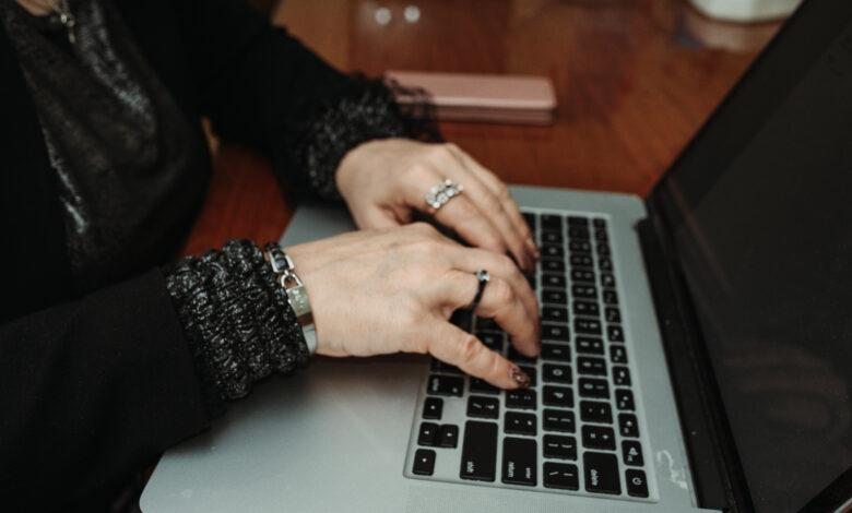 Close-up of hands typing on a laptop at a wooden table