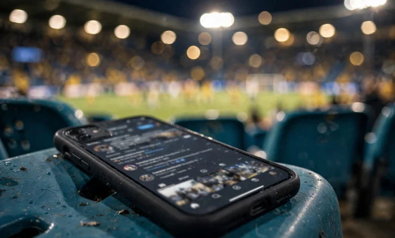 Smartphone displaying a generic football social media feed in a stadium crowd during a night match
